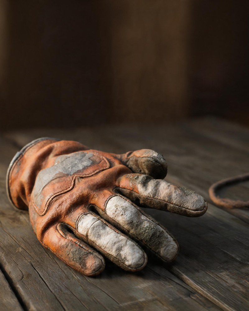 A heavy stitched work glove lying on planks, fingers still curled around the shape of a tool that is not there.